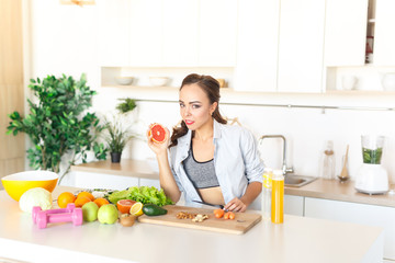 young beautiful girl cuts grapefruit to prepare fresh juice in the kitchen