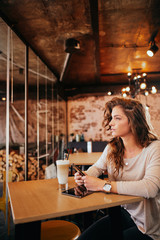 Woman using smart phone and drinking coffee while sitting in cafe.