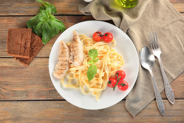 Plate of delicious pasta with grilled chicken fillet and tomatoes on table, top view