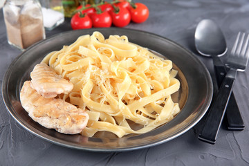 Plate of delicious pasta with cheese and grilled chicken fillet on table