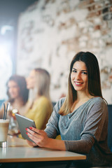 Young caucasian woman using tablet while sitting in cafe and drinking coffee.