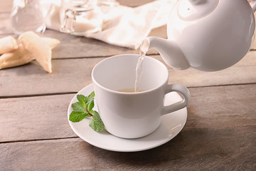 Pouring of hot aromatic tea into cup on table