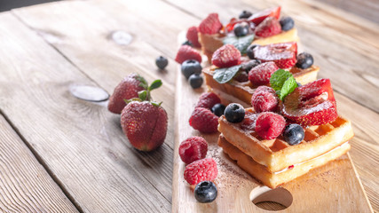 Viennese waffles with strawberry jam, fresh strawberries, raspberries, blueberries and chocolate chips on a wooden table. Delicious breakfast concept