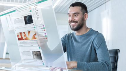 In the Near Future Stylish Man Using His High-Tech Computer with Transparent Display For Social Networking. He Sits at the Table in Light Modern Room and Smiling.