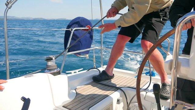 Male hands pulling blacke rope winded round side winch while making a turn. Filmed on sailing trip in Croatia in slow motion hd.