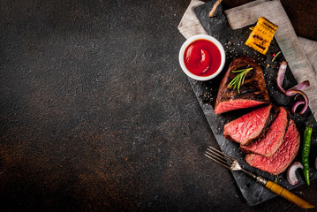 Fresh grilled beef, homemade bbq meat medium rare, on black stone cutting board, with spices, dark background, copy space above
