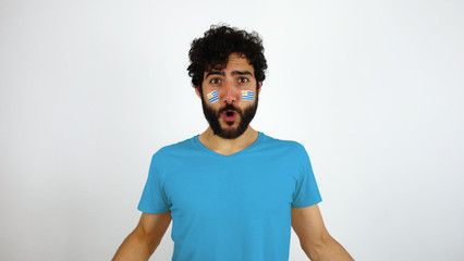 Sport fan celebrating a goal of his team. Man with the flag of Uruguay makeup on his face and blue...