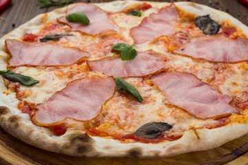 Delicious italian pizza with ham and basil leaves on wooden background