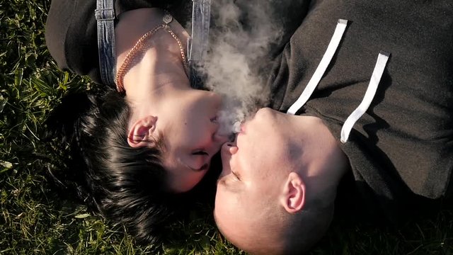Young Guy and Girl smoke kiss e-cigarette Vape and Kissing in a Park Picnic Day 