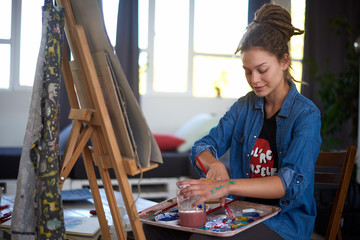 Naklejka premium Artistic girl sitting in studio and paint on easel.