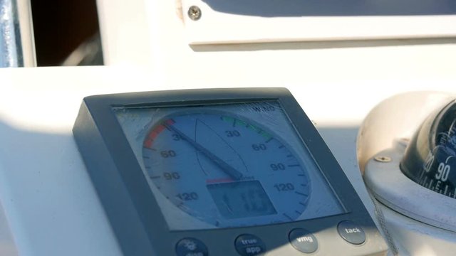 Sailing boats instrument by the steering wheel showing wind direction and speed. Closeup on windex and some rotating blurred steering wheel.