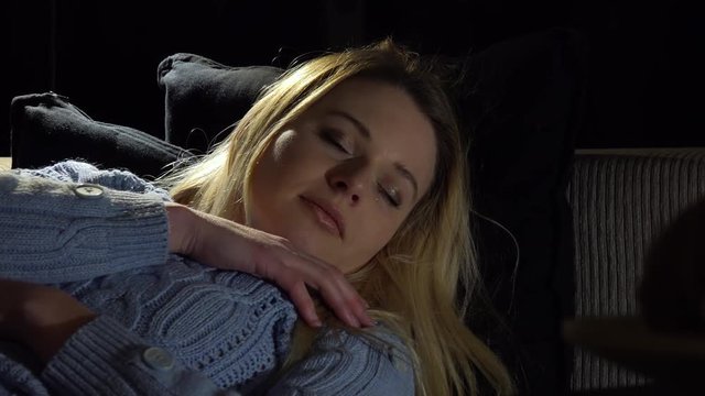 A young beautiful woman sleeps on a couch in a dark room - closeup