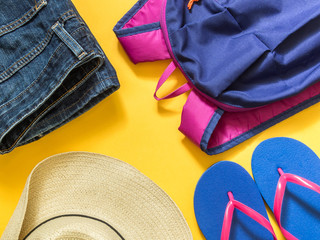 Travel vacation background. Flip flops, backpack, jeans, hat on a yellow background. Flat lay