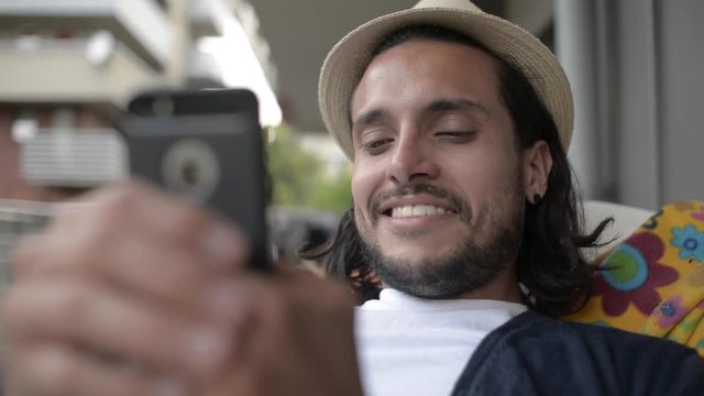 Young Latin Guy use Mobile Smart Phone to Communicate sitting at Home Backyard