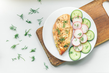 Baked chicken breast with cheese, cucumber and red radish on white plate. Healthy diet protein food.
