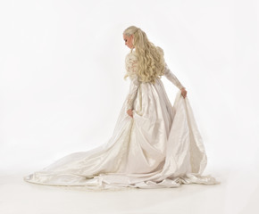 full length portrait of blonde woman wearing long white bridal gown. standing pose on white studio background.