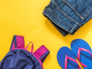 Travel vacation background. Flip flops, backpack, jeans on a yellow background. Flat lay