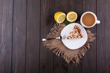 Cup of tea with milk and piece of lemon pue served on dark wooden table