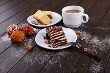 Breakfast. Cup of tea with milk and two plates with cheesecake and chocolate cake served on wooden table