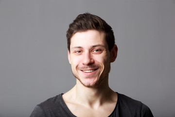 Obraz premium Close up horizontal portrait of young man smiling against gray background