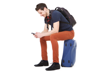happy male traveler sitting on suitcase and looking at cellphone