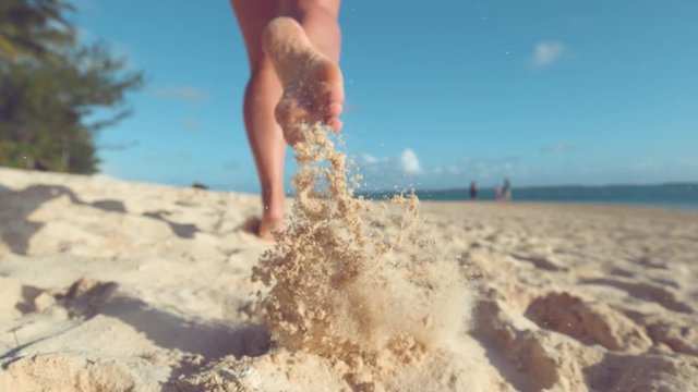 SLOW MOTION:, LOW ANGLE, CLOSE UP, DOF Unrecognizable woman running in the hot summer sun along the sunny exotic shore in Cook Islands. Carefree girl takes off her flip flops and runs in the sand.