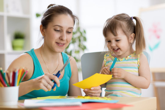 Mom helping her child daughter to cut colored paper