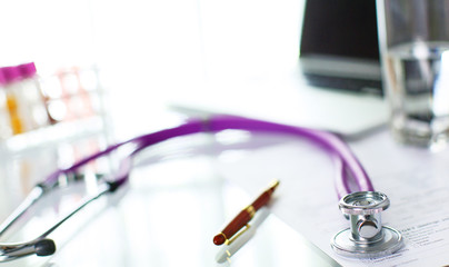 closeup of the desk of a doctors office with a stethoscope in the foreground and a bottle with pills in the background, selective focus