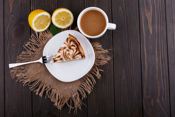 Cup of tea with milk and piece of lemon pue served on dark wooden table