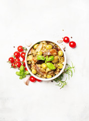 Stewed aubergines with vegetables and herbs in a bowl, light background, top view