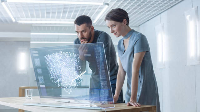 In the Near Future Male and Female Computer Engineers Talk While Working on the Transparent Display Computer. Screen Shows Interactive Neural Network Project, Futuristic User Interface.