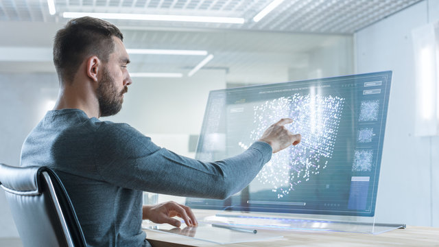 In the Near Future Man Working on His Computer with Transparent Display. Display Shows Graphic Projection of Neural Network, Artificial Intelligence Simulation.