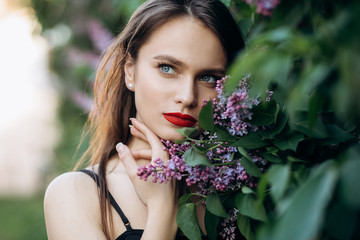 The charming girl stands near bushes with flowers