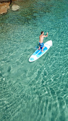Fototapeta premium Aerial drone bird's eye view of a man exercising sup board in turquoise tropical clear waters at sunset
