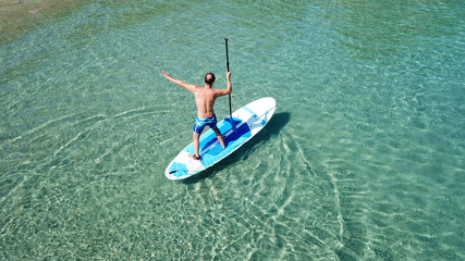 Fototapeta premium Aerial drone bird's eye view of a man exercising sup board in turquoise tropical clear waters at sunset