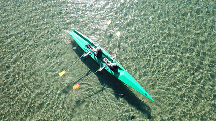 Aerial drone bird's eye view of sport canoe operated by 2 young women in turquoise clear waters