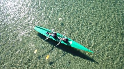 Aerial drone bird's eye view of sport canoe operated by 2 young women in turquoise clear waters