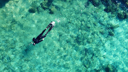 Naklejka na ściany i meble Aerial drone bird's eye view photo of scuba diver in tropical rocky sea with turquoise clear waters