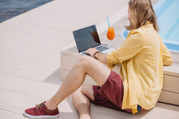 young man using laptop with blank screen while sitting at poolside