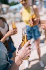 cropped shot of young people drinking beer at sunny summer day on beach