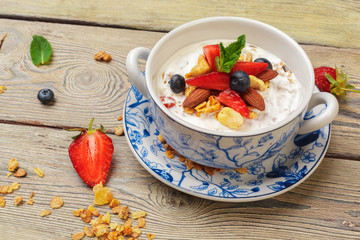 Bowl of homemade granola with yogurt and fresh berries on wooden background