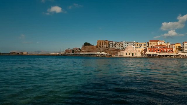 Tracking shot of the Old Town promenade in Chania, Crete, Greece with the Mosque of the Janissaries progressively lit by the sun