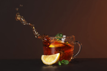 Glass cup and splash of delicious lemon tea with mint on table against color background