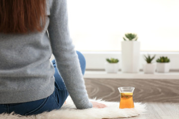 Cup of hot tea and woman sitting on floor at home