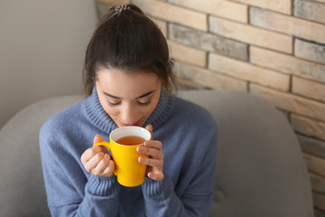 Beautiful young woman with cup of hot tea at home