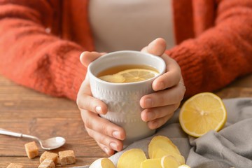 Woman holding cup of tea with lemon and ginger on wooden table