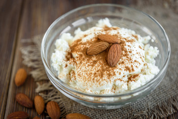 Cottage cheese with sour cream, cinnamon and almond on dark wooden background. Healthy diet food. Protein meal.