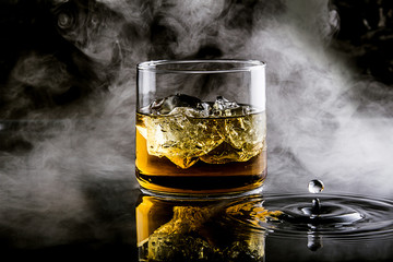 whiskey with ice on black background with splashes of water and smoke