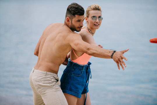 beautiful happy young couple throwing flying disc on beach