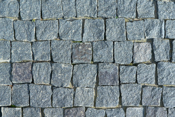 The pavement laid with square stone cobbles of granite. Rough stones, rough. The shape of the stones is uneven and square. Color dark gray. Background, texture or backdrop.